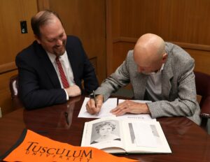David Nyholm, right, signs the scholarship document while Dr. David Cook watches. A photo of Nyholm’s wife, June, is in the foreground.