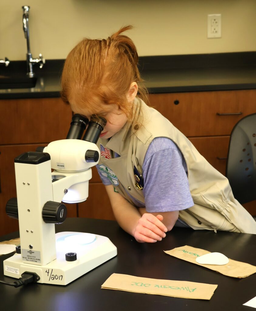 A Girl Scout peers through a microscope.