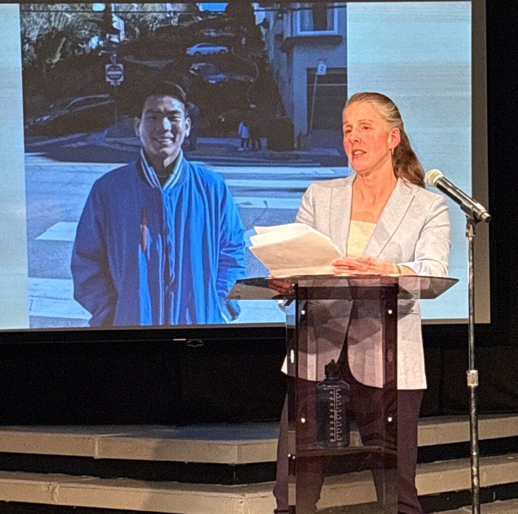 Kelsey Trom speaks as a photo of alumnus Ethan Lau displays in the background.