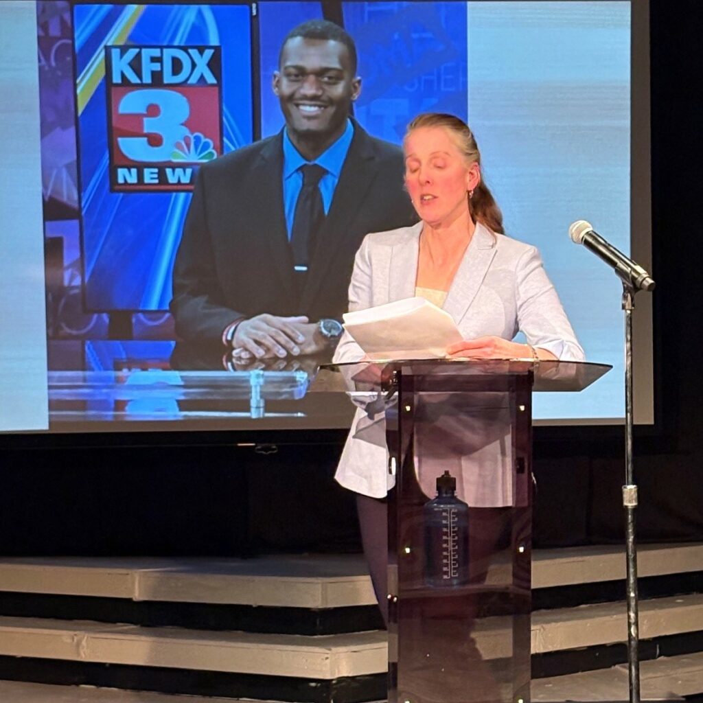 Kelsey Trom speaks as a photo of alumnus PJ Green displays in the background.