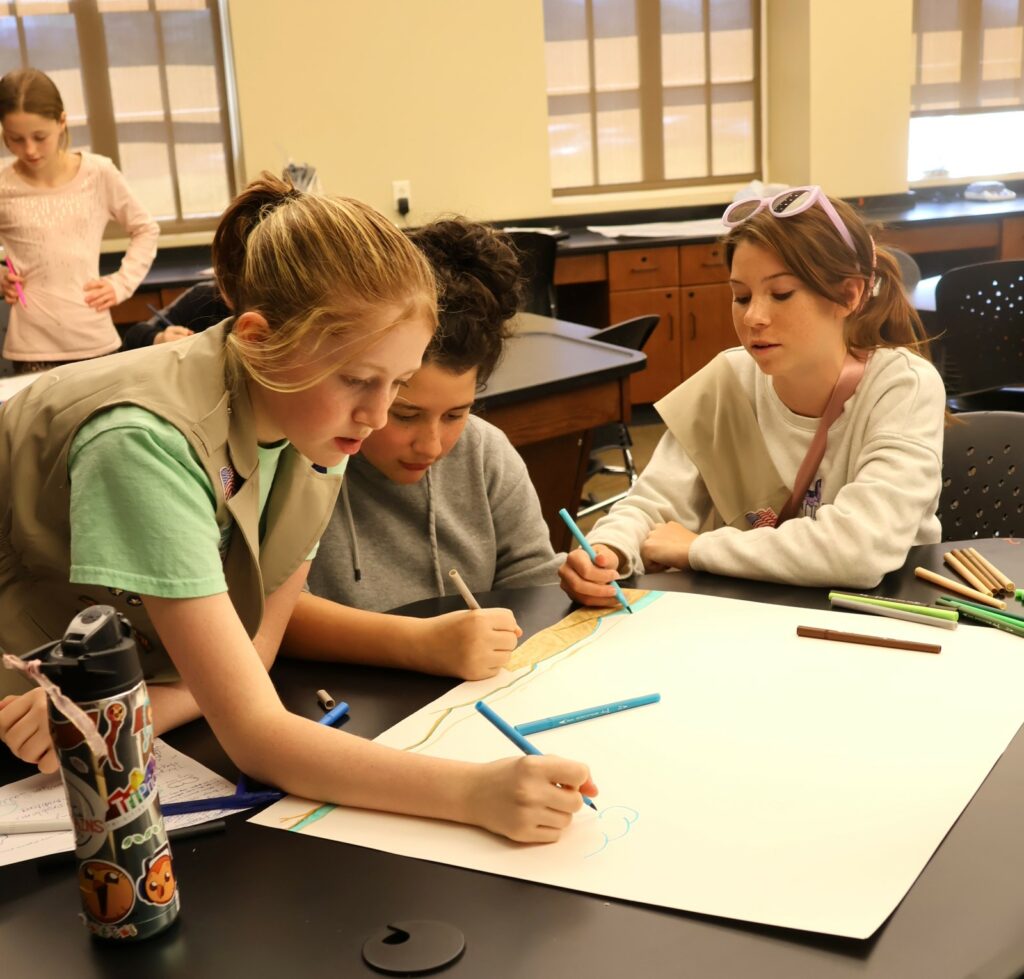 Three Girl Scouts work on their poster.