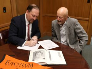 Dr. David Cook, left, signs the scholarship document while David Nyholm observes.