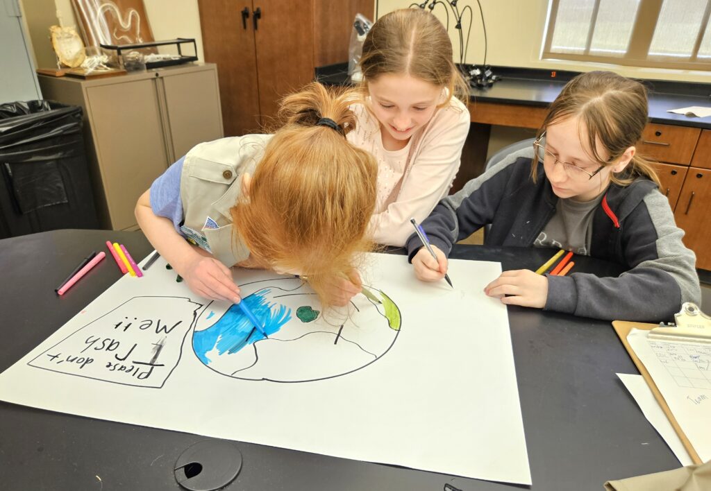 Three Girl Scouts work on their poster.