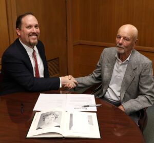 Dr. David Cook, left, and David Nyholm shake hands before signing the document.