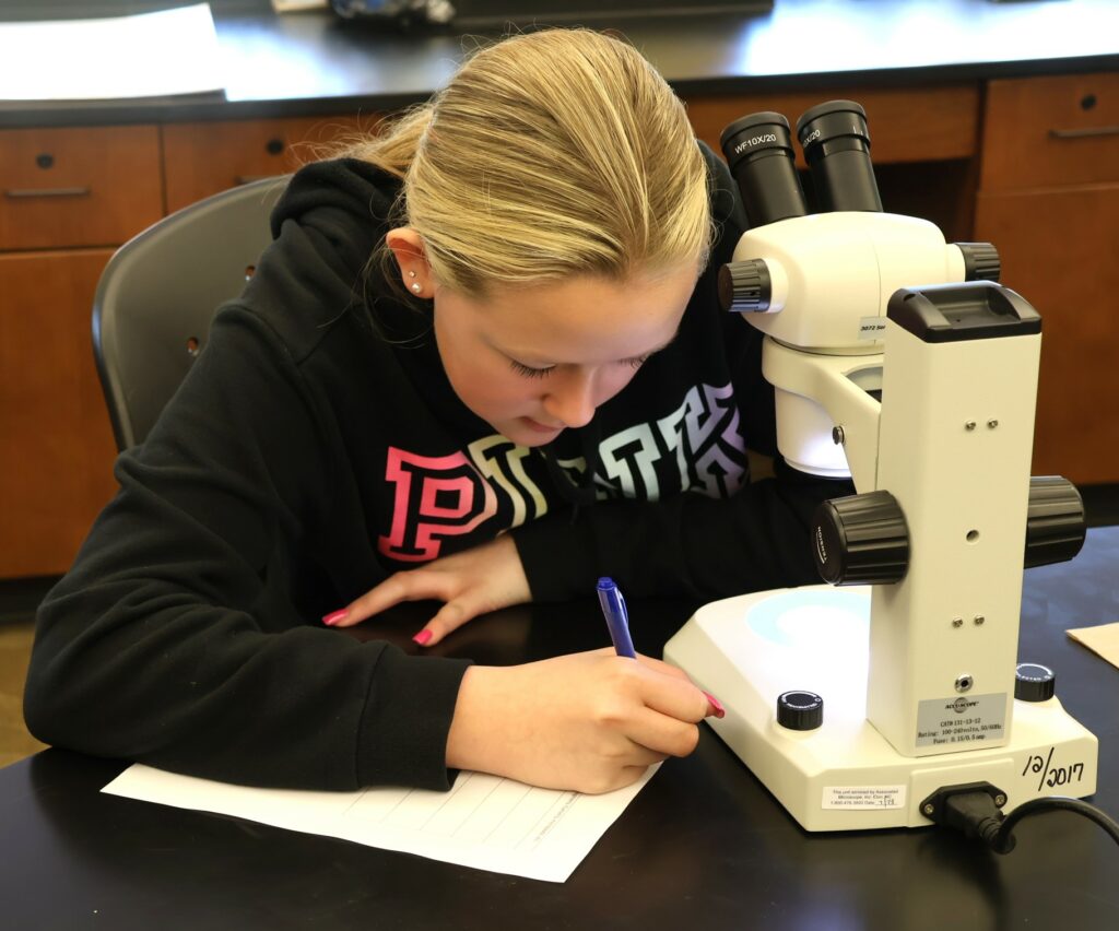 A Girl Scout writes something as she works on her microplastics project.