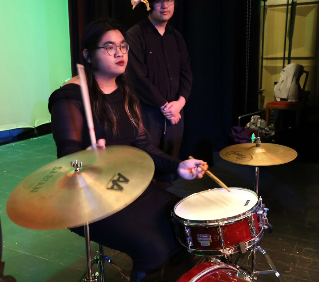 A band member plays the drum and cymbals.