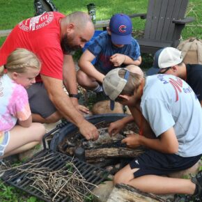 Dr. Peter Noll, second from left, helps participants in the Pioneer Skills Camp start a fire in 2024.