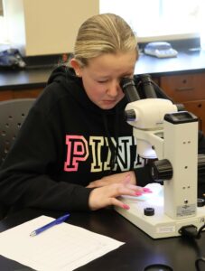 A Girl Scout looks at a filtered water sample under a microscope.