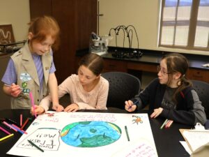 Three Girl Scouts work on their poster.