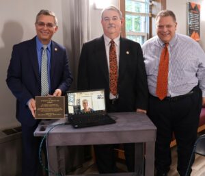 Top row, left to right, Dr. Scott Hummel, Tusculum’s president, Dr. Greg Nelson, chair of the Board of Trustees; and Edward Roberts, vice president of institutional advancement, stand as Janet Welty watches via Zoom. Dr. Hummel is holding the plaque for the Stanley R. Welty Jr. Lobby.