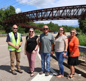 Left to right, Danny Greene, the City of Tusculum’s police chief, Dr. Melissa Bryant, director of alumni relations for the university; Tusculum Mayor Alan Corley; Carrie Maggert, vice president of operations at the university; and Kim Collins, executive assistant to the president at the university, stand in front of the bridge where the sign will be placed.