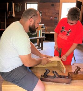 Dr. Peter Noll, left, assists one of the participates in the Woodworking Camp in 2023.