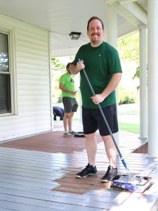 Dr. David Cook stands on the porch of the male house for the Discipleship Living-Learning Center and prepares to paint a section of it.