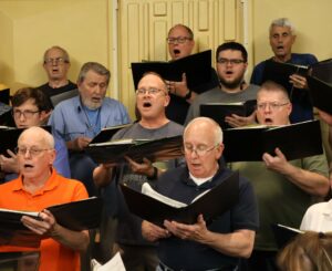 Male chorus members sing during rehearsal for the upcoming concert.