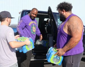 Tusculum staff member Steve Anderson, center, and student Xavier Velazquez, right, and a community member load bottled water in a car.