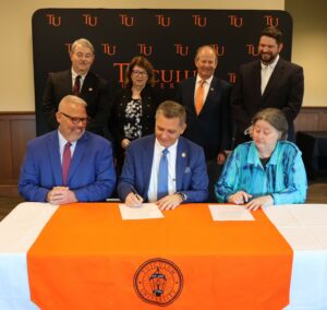 Dr. Scott Hummel, Tusculum’s president, front and center, and the Rev. Diana Moore, front right, sign the updated covenant as the Rev. Rodney Norris, front left, watches. On the back row are, left to right, Dr. Greg Nelson, the Rev. Karen Russell, Dr. Dan Donaldson and Dr. Chris Shumate.