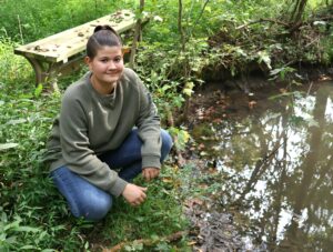 Tusculum student Breanna Mathes crouches by the pond where she and Joe Calloway first discovered the blue crayfish.
