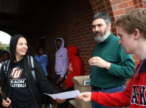 Student Joseph Medeck, right, hands out an informational sheet to fellow Pioneer Brynn Smith, left, as Dr. Chuck Pearson, middle, mans the eclipse glasses box.