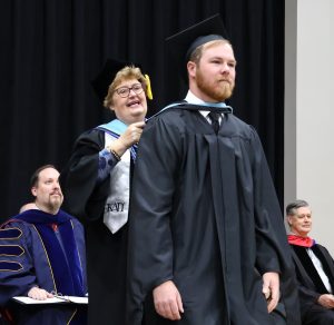 Dalton Ramsey, the graduate student speaker, is hooded by Dr. Peggy Goodson-Rochelle during commencement.