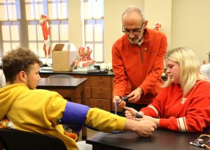 Elijah Ramos, left, and Kayleigh Cook, right, learn about blood pressure from Dr. Wilton Remigio, their biology professor.